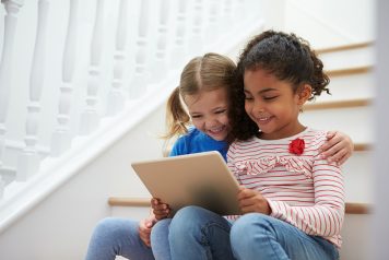 Two small children smiling and looking at a tablet computer together at home