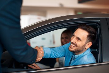 Man shaking hands with car salesman through window