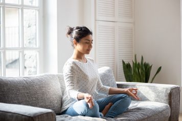 Woman meditating in lotus position on couch at home