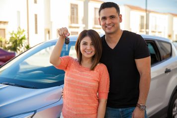 Couple smiling and holding new car keys in front of new car