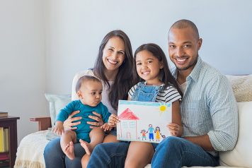 Young family sitting on couch holding child's drawing of new house