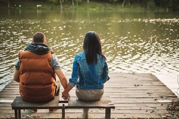 Couple holding hands on a bench and sitting near a lake talking