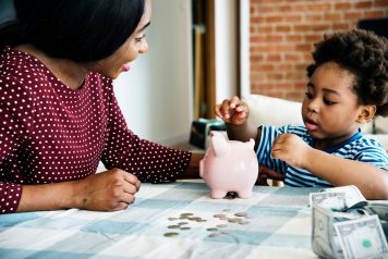Mom with her daughter collecting coins into the piggy bank.