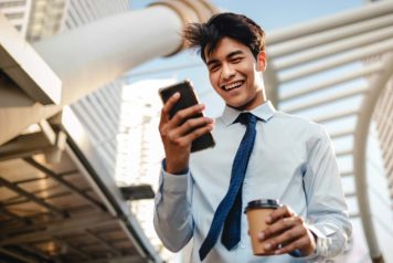 Man looking at his smartphone smiling with a coffee