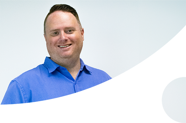 Man smiling and standing in front of white backdrop in blue shirt